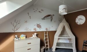 Babykamer met wit ledikant onder hemelbed, muurschildering met zeeschildpadden en koraal op schuine wand