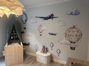 Babykamer met houten ledikant, hemeltje en muurstickers van luchtballons, vliegtuigen en wolken in vintage stijl