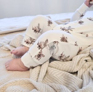 Baby in crèmekleurige pyjama met rendierprint op bed met beige deken
