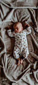 Slapende baby in pyjama met regenboogprint op beige fleece deken met armen gestrekt