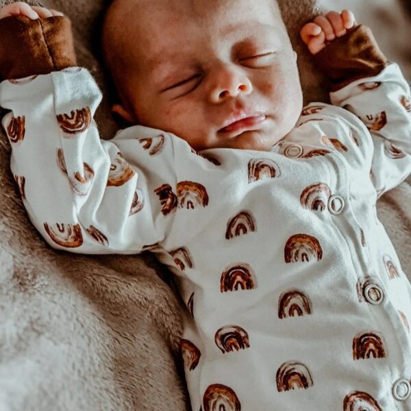 Slapende pasgeboren baby in witte romper met regenboogprint op zachte bruine deken