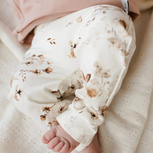 Baby in roze shirt met witte broek met bruin bloemenpatroon liggend op gestippelde deken