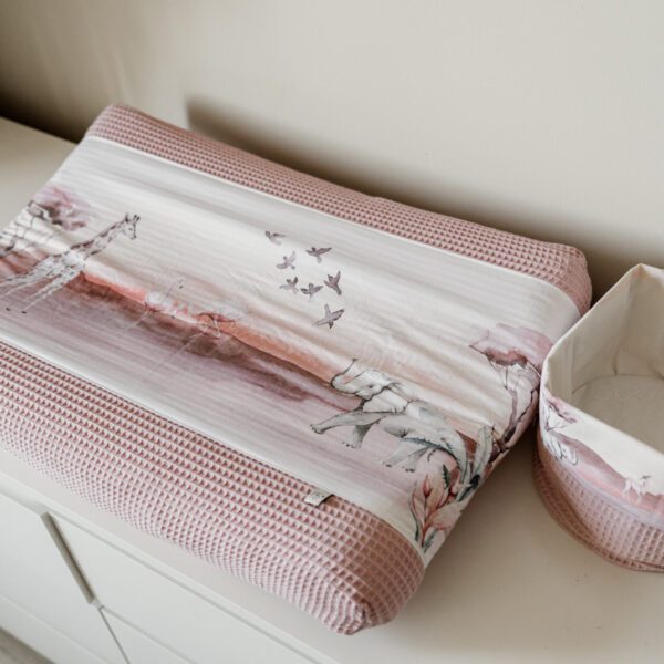 Roze aankleedkussen met dierenprint en bijpassend mandje op witte commode in babykamer