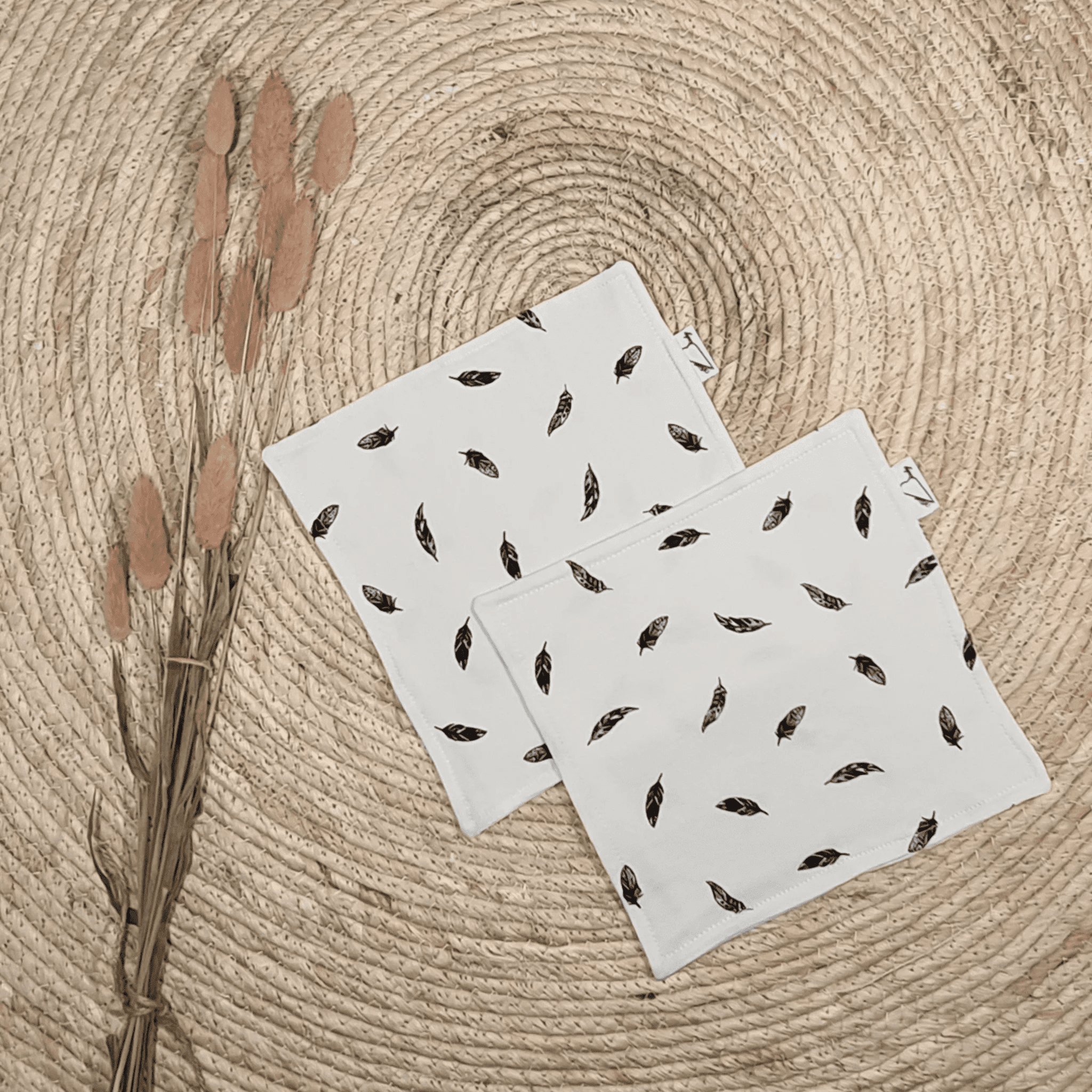 Drie witte stoffen zakjes met zwart verenpatroon op rond gevlochten juten placemat met droogbloemen