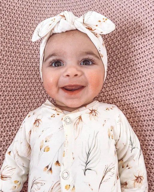 Lachende baby met witte strik haarband en bloemenmotief kleding op roze gebreide deken