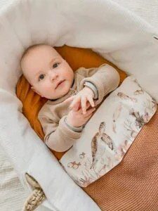 Baby ligt in wiegje met beige trui en deken met safaridieren print in aardetinten