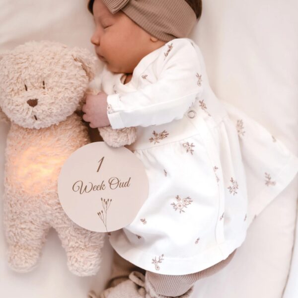 Slapende baby met taupe haarband en pluchen knuffel, met mijlpaalkaart '1 Week Oud