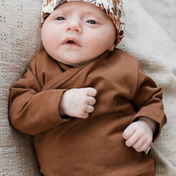 Baby in bruine overslagshirt met gebloemde muts en broek op gebreide deken