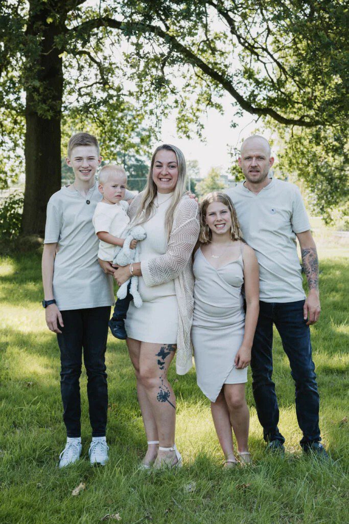 Gezinsportret van ouders met drie kinderen in het park onder groene bomen op zonnige dag