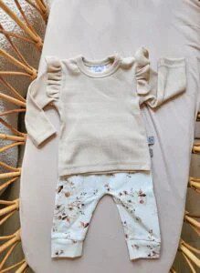Beige babyshirt met ruches en broekje met bloemenprint op rieten stoel