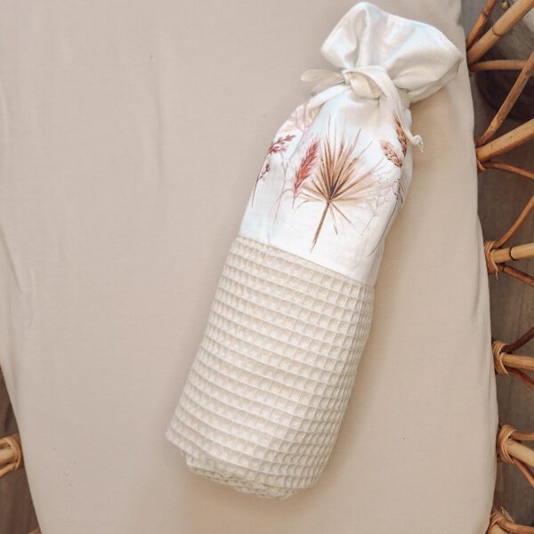 Witte wafelkatoenen handdoek met gedroogde bloemen in linnenzak op rieten stoel
