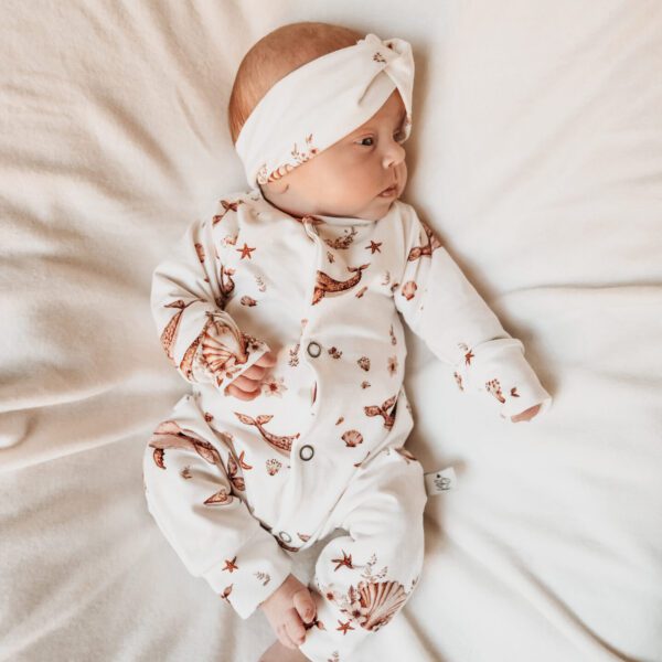Baby liggend op beige deken in wit pakje met schelpen print en bijpassende haarband
