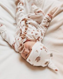 Pasgeboren baby in witte omslagdoek met bruine dierenprint en houten bijtketting op beige deken