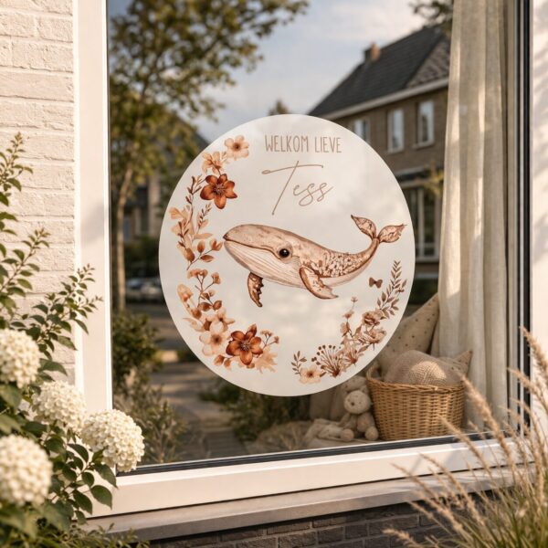 Raamsticker met walvis en bloemen met tekst 'Welkom lieve Tess' op raam in woonwijk