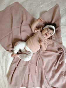 Baby liggend op beige deken met haarbandje en broekje met bloemenmotief in neutrale tinten