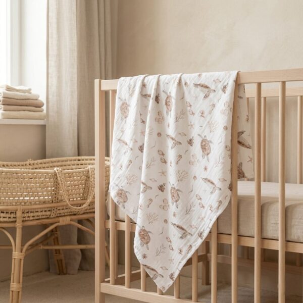 Houten babybedje met witte deken met zeedieren print en rieten wiegje in neutrale babykamer