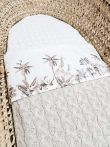 Wit babydekentje met safari print van giraffe, neushoorn en olifant tussen palmbomen op rieten mand