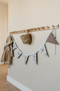 Houten kapstok met v-vormige haken, decoratieve slinger, rieten mandje en textiel in neutrale tinten