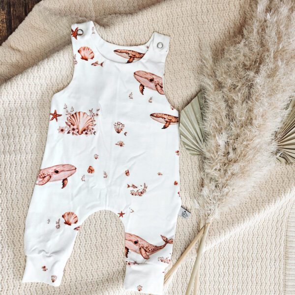 Witte baby romper met oceaan print van walvissen, schelpen en zeesterren op beige deken met droogbloemen