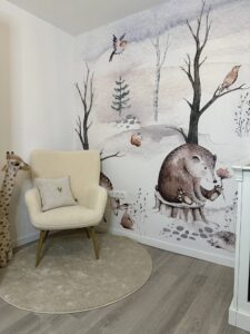 Babykamer met wandschildering van bosdieren, beer, vogels en egel met crèmekleurige fauteuil en giraf knuffel