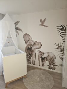 Babykamer met wit ledikant en muurschildering van olifanten, papegaai en palmbladeren in sepia tinten