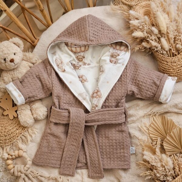 Roze baby badjas met teddybeer print en bijpassende accessoires op natuurlijke achtergrond met droogbloemen