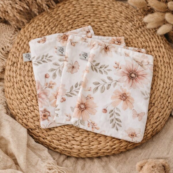 Twee katoenen hydrofiele doeken met vintage bloemenprint op gevlochten rieten mand met beige dekentje