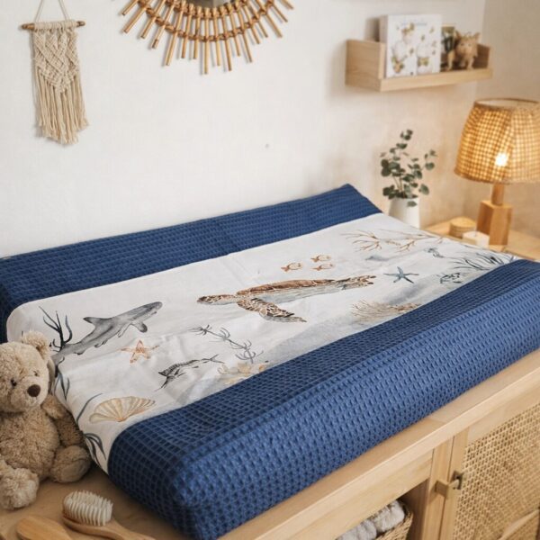 Babylkamer met houten commode, blauwe aankleedkussen en rotan spiegel boven macramé wandhanger