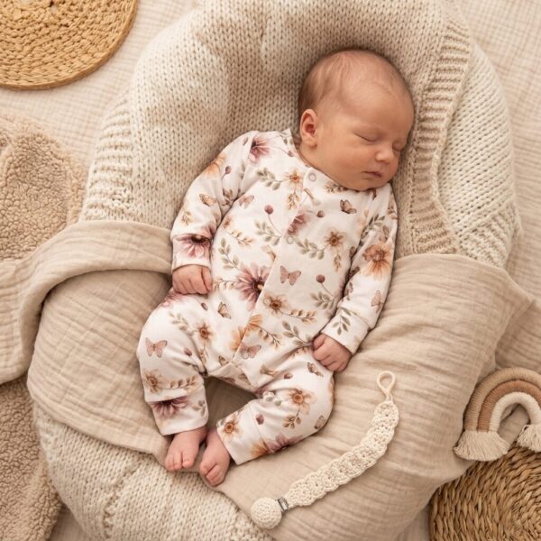 Slapende baby in bloemenpyjama op beige gebreide kussen met natuurlijke accessoires