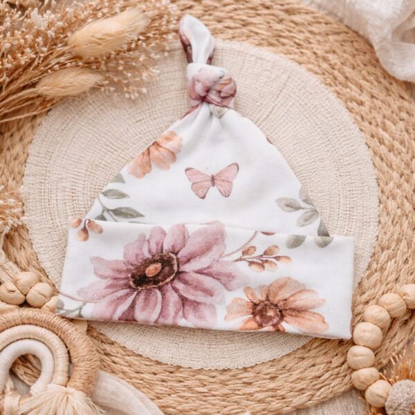 Babymuts met roze bloemenprint en vlindermotief op rieten ondergrond met droogbloemen en houten speelgoed