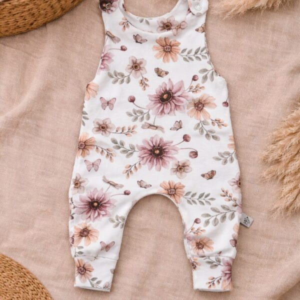Wit babyrompertje met roze bloemenprint en vlinders op beige ondergrond met droogbloemen en rieten manden