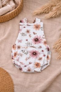 Witte baby romper met roze en oranje bloemenprint en vlindermotief op beige ondergrond met rieten manden