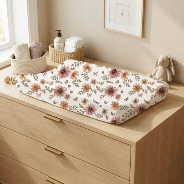 Aankleedkussen met bloemenpatroon op houten commode in neutrale babykamer met opbergmandjes en knuffel