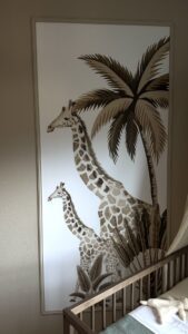 Wanddecoratie met twee giraffen en palmbladeren in bruine tinten op witte achtergrond naast babybedje